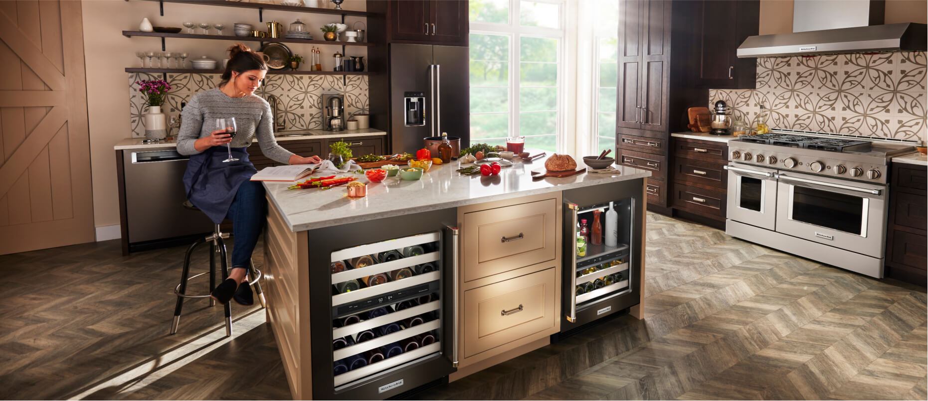 A person sitting at the island of a bold, modern kitchen, outfitted with a suite of KitchenAid® appliances.
